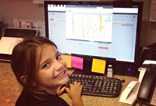 Child smiling, using a computer on desk.