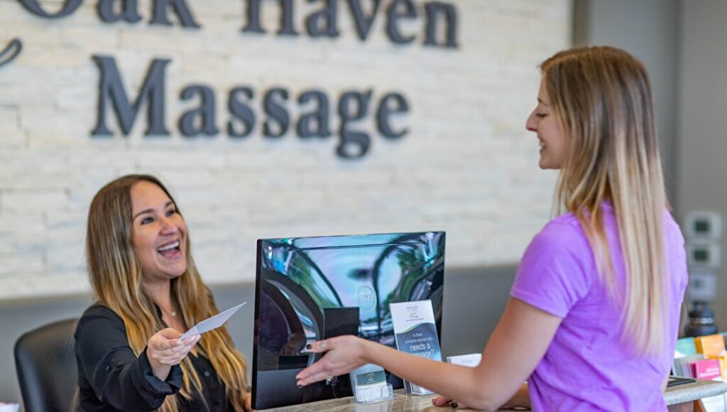 Smiling receptionist handing paper to customer at massage center.