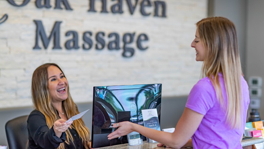 oak haven frontdesk 01 Smiling receptionist handing paper to customer at massage center.
